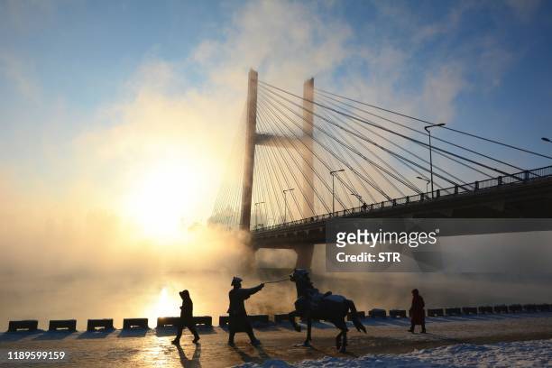 This photo taken on December 18, 2019 shows people walking past a statue of a horse amid fog over the Songhua river in Jilin city in China's...