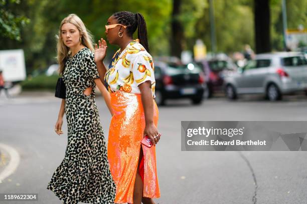 Guest wears earrings, a keyhole black spotted pattern beige ruffled dress with puff sleeves ; A guest wears earrings, Gucci orange sunglasses, a...