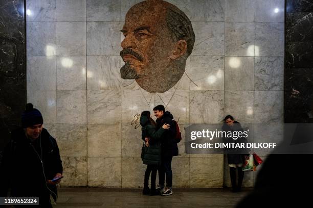 Couple hugs as they stand in front of a mosaic depicting former Soviet leader Vladimir Lenin at Biblioteka Imeni Lenina metro station in Moscow on...