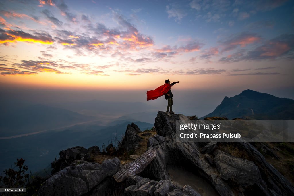 Success, leadership, achievement and people concept - silhouette of businessman with flag on mountain top over sky and sun light background