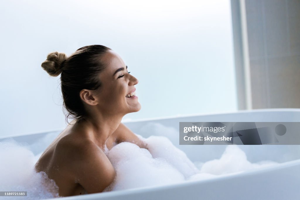 Joven mujer feliz disfrutando en el baño de burbujas con los ojos cerrados.