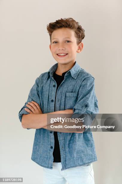 lachende jongen staande met armen gekruist tegen een grijze achtergrond - kids fashion stockfoto's en -beelden