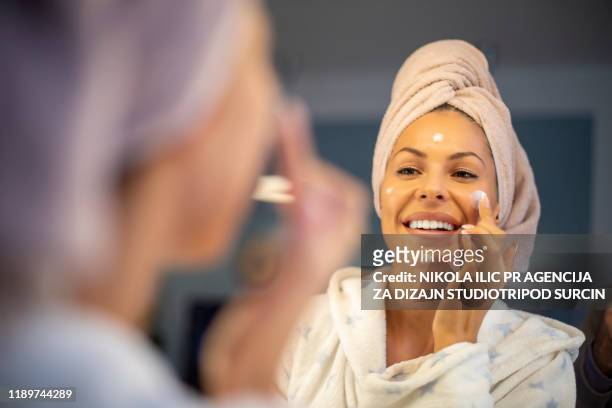 young woman applying face cream. - face cream stock pictures, royalty-free photos & images