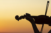silhouette of a wooden violin in female hands, the figure of a stringed musical instrument on a sunset sky, the concept of music and art