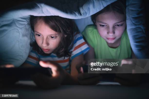 niño y niña jugando juegos en el teléfono móvil en su cama - esclavitud fotografías e imágenes de stock