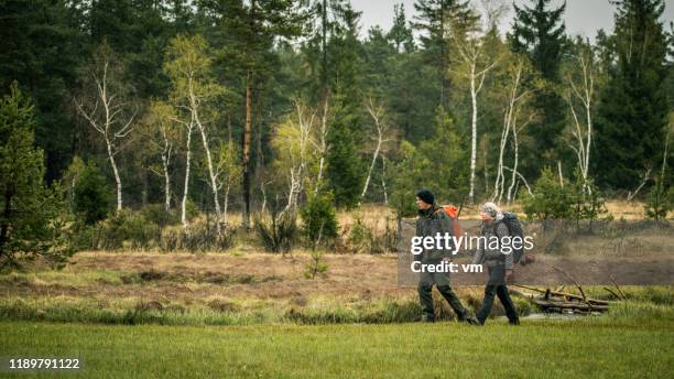 hiker couple walking across a meadow - survivalist stock pictures, royalty-free photos & images