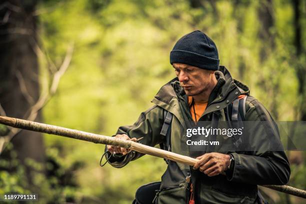 überlebensmensch schärft einen stock in einem wald - überlebenskünstler stock-fotos und bilder