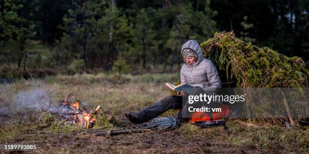 woman sitting next to a campfire and reading a book in nature - wilderness stock pictures, royalty-free photos & images