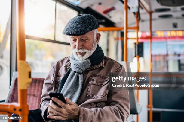 foto van volwassen zakenman die met de bus in de stad reist tijdens de winterdag. senior man met baard reizen met de bus en met behulp van zijn slimme telefoon - travel real people stockfoto's en -beelden