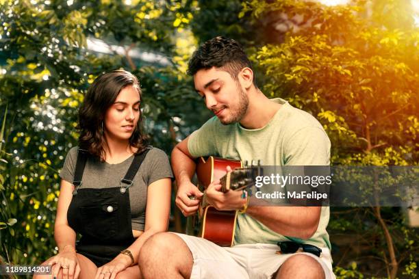joven tocando la guitarra acústica para una chica hermosa - serenata fotografías e imágenes de stock