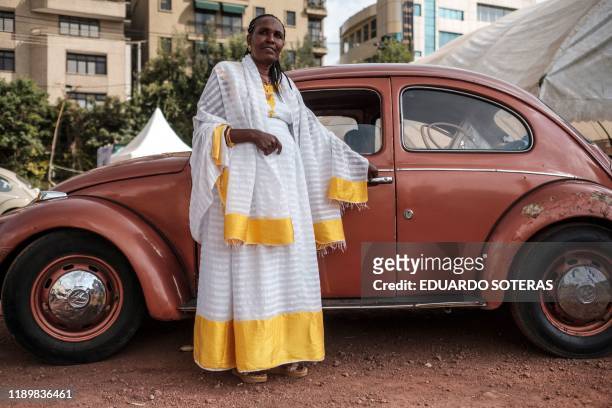 Woman wearing traditional Ethiopian clothes stands next to a VW Beetle car during the first event gathering owners of classic Volkswagen owners, in...