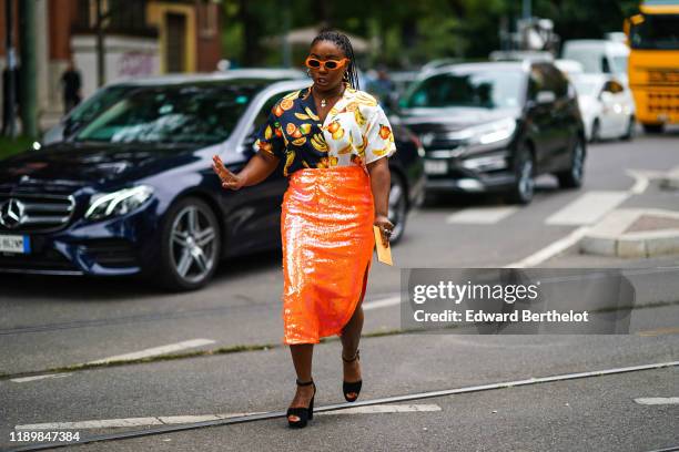 Guest wears orange Gucci sunglasses, earrings, necklaces, a half-white half-black shirt with a yellow, orange and green fruit pattern, an orange...