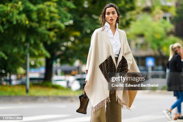 Guest wears a white shirt, a cream-color fringed Fendi poncho, a camel bag, light brown pants, outside the Fendi show during Milan Fashion Week...
