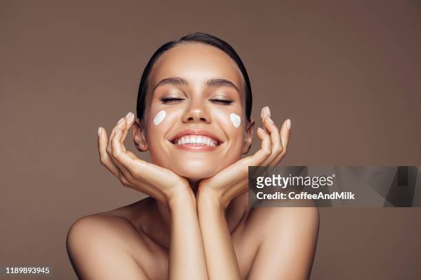 beautiful woman applying cream on her face - human skin stock pictures, royalty-free photos & images