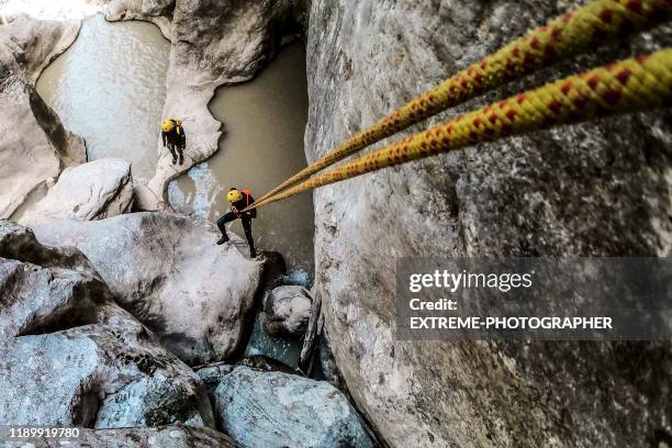 high angle view of canyoneers making a descend in a canyon using a rope that is adjacent to the camera - adventure sports stock pictures, royalty-free photos & images