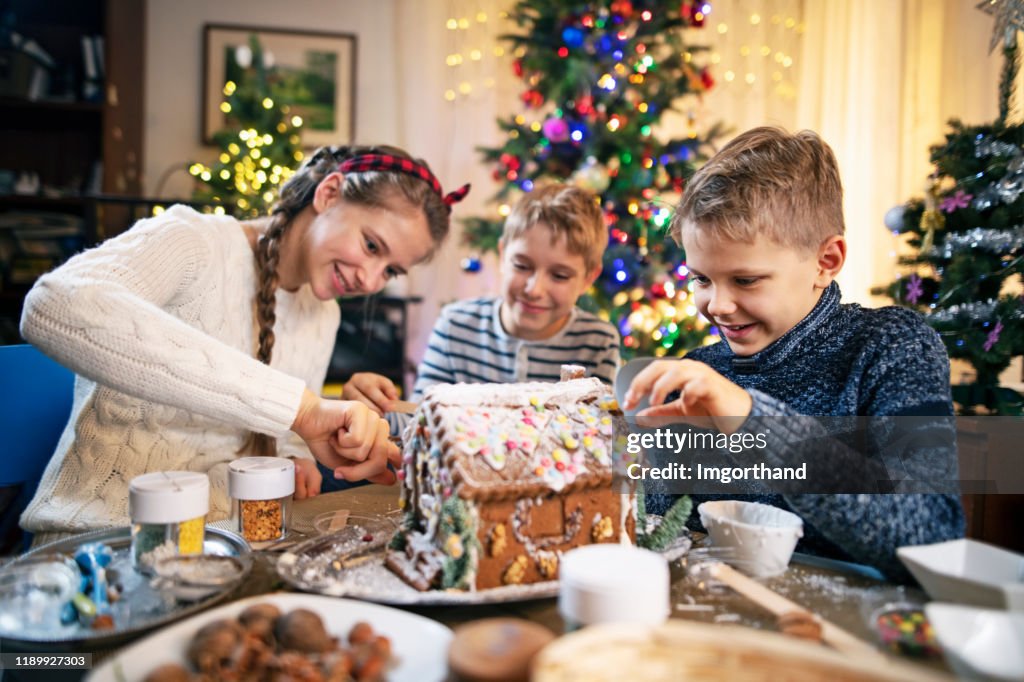 Mother and kids enjoying decorating gingerbread house for Christmas