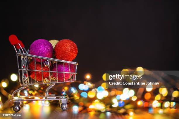 mini shopping cart against christmas lights background - shopping trolleys stockfoto's en -beelden