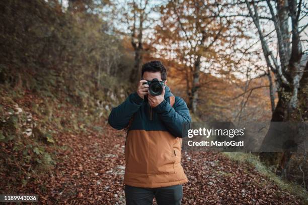 young man using a dslr camera in a forest in autumn - digital-single-lens-reflex-camera stock pictures, royalty-free photos & images
