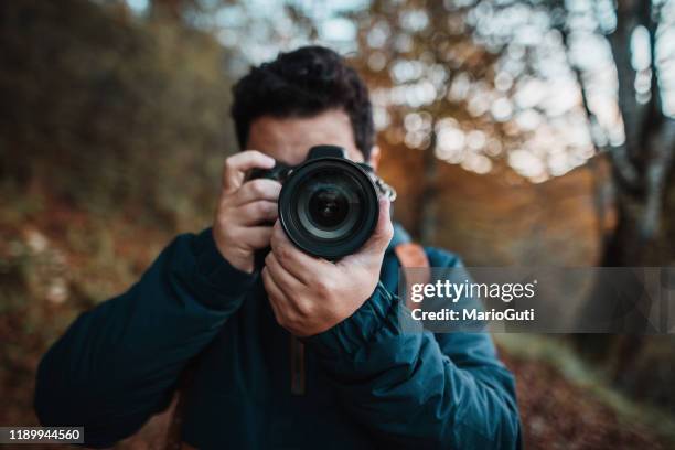jonge man met behulp van een dslr-camera in een bos in de herfst - spiegelreflexcamera stockfoto's en -beelden