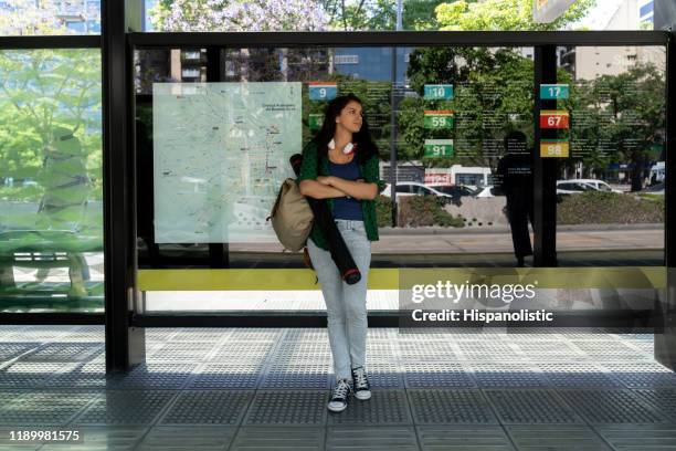 latin american student at the bus stop waiting - city lifestyles - bus shelter stock pictures, royalty-free photos & images