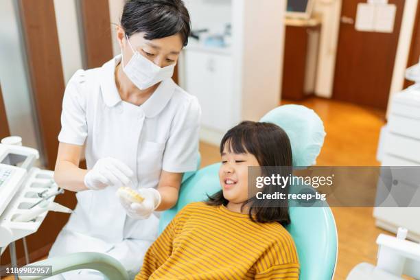 ragazza dal dentista che ascolta la spiegazione sui suoi denti - dentista bambini foto e immagini stock
