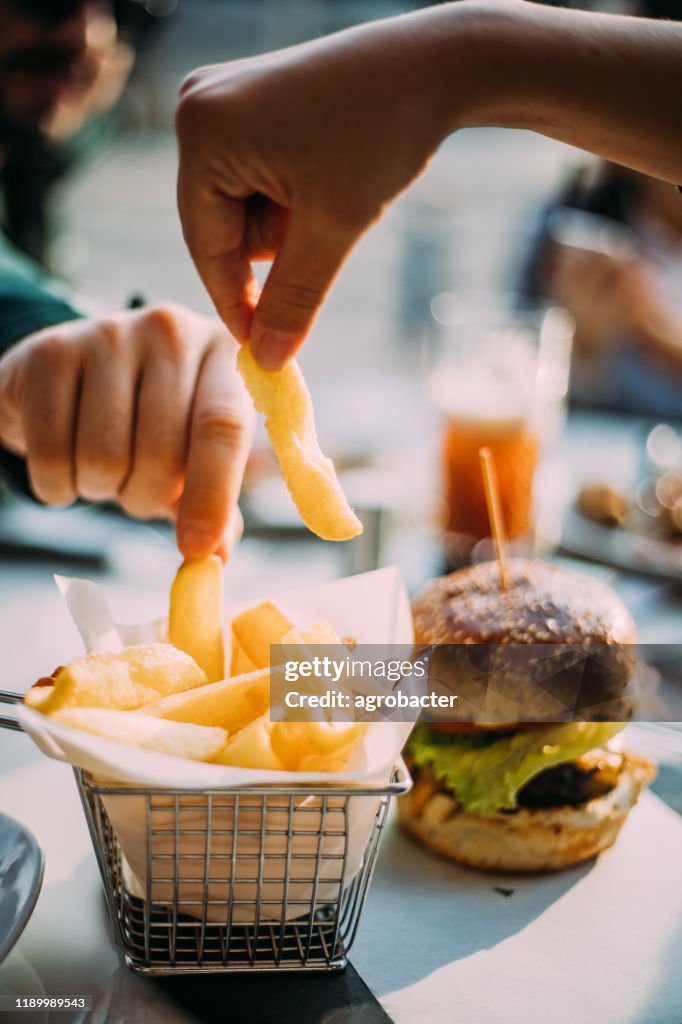 Hands of two young people sharing bowl of french fries