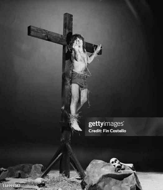 English musician Michael Burston , aka Wurzel, the guitarist from heavy metal band Motorhead, flips the bird whilst tied to a crucifix in a London...