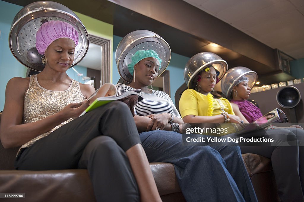 Women friends sitting under hair dryers at salon
