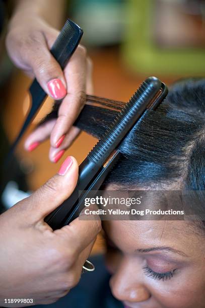 woman getting hair straightened in salon - hairdressers black woman stock-fotos und bilder