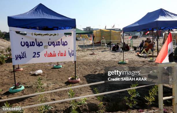 Iraqi anti-government protesters rest in a tent displaying a banner honouring demonstrators who died in ongoing rallies, on the bank of the Tigris...