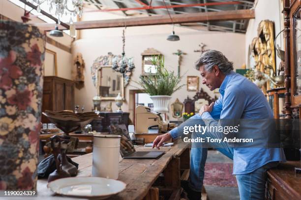 mature male owner of antique store using laptop in his shop - antique shop stock pictures, royalty-free photos & images