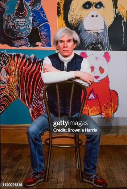 Portrait of American Pop artist Andy Warhol as he sits backwards on a chair in his Union Square studio, the Factory, , New York, New York, 1982.