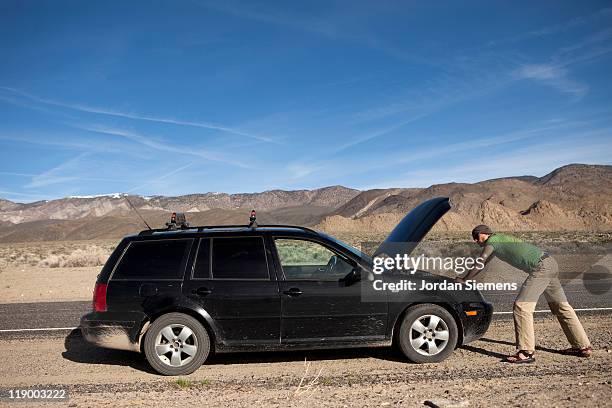 man standing near a broke down car. - beat up car stock pictures, royalty-free photos & images