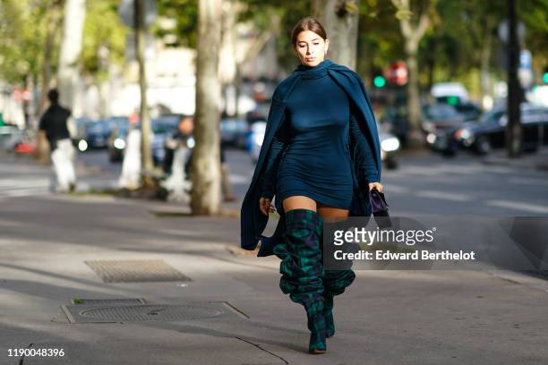 Guest wears a blue dress, a cape, thigh high ruffle boots with green and blue printed checked patterns, outside Alessandra Rich, during Paris Fashion...