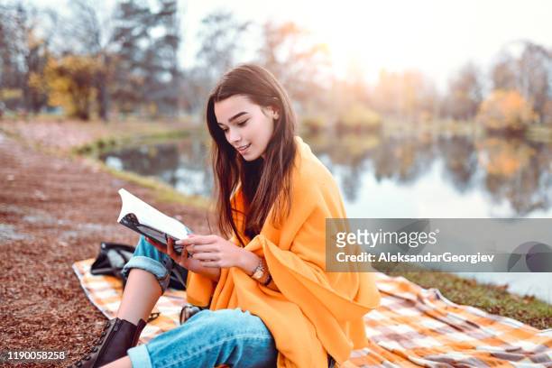 cute female reading a book in park - literature stock pictures, royalty-free photos & images