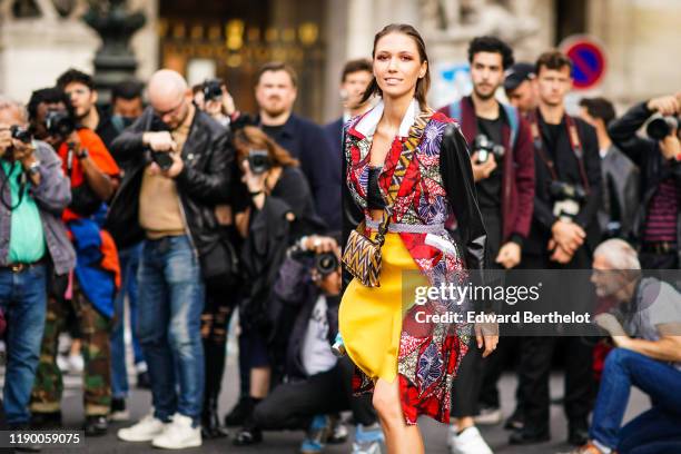 Landiana Cerciu wears a yellow skirt, a multicolor floral print top with black sleeves, and poses in front of several photographers, outside Balmain,...