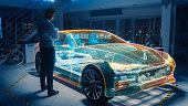 In Automotive Innovation Facility Automobile Design Engineer Working on 3D Holographic Model Projection of Electric Car. Futuristic Concept of Virtual and Augmented Realty Use.