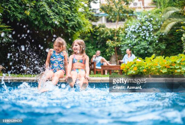 junge mädchen spritzen pool wasser mit beinen - seite an seite stock-fotos und bilder