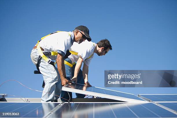 two men lifting a solar panel - positionner photos et images de collection