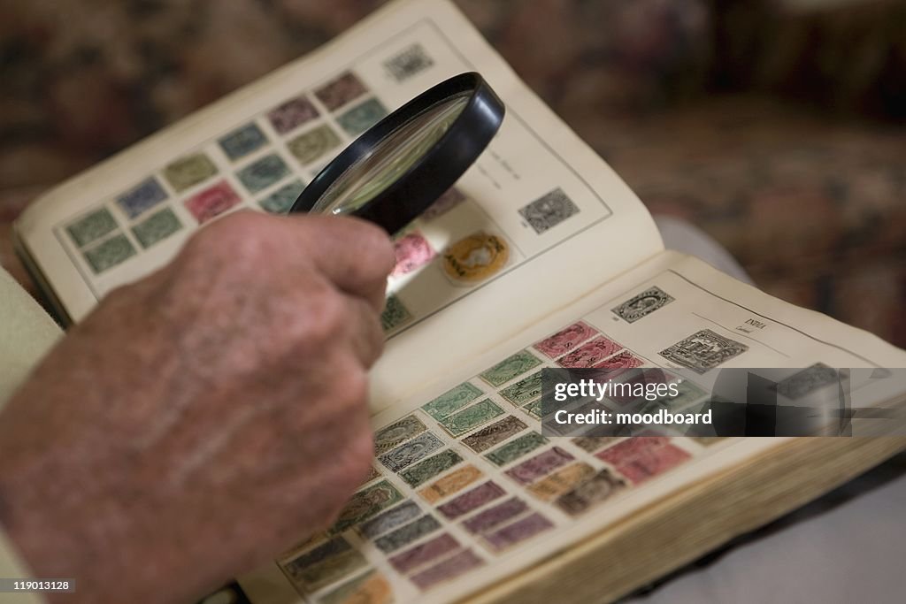 Senior man looks at stamp collection with magnifying glass