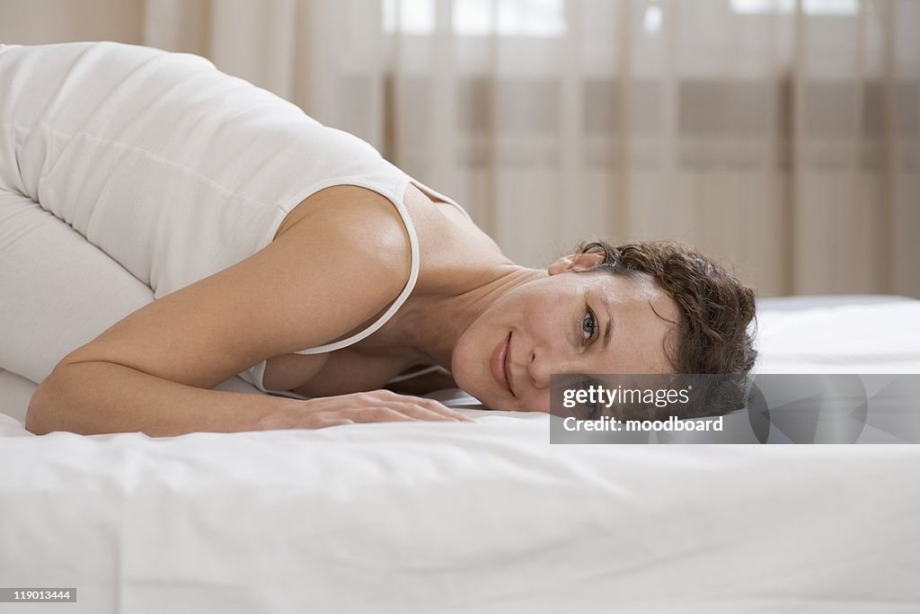 Mid adult woman kneels on bed smiling at camera
