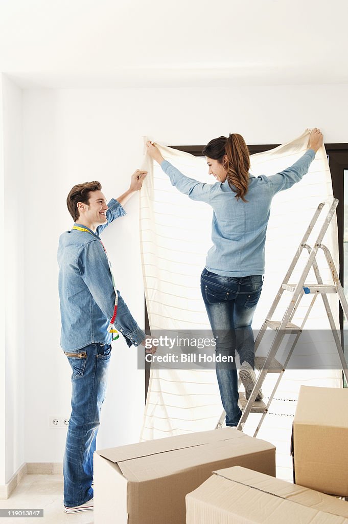 Couple hanging curtain in new home