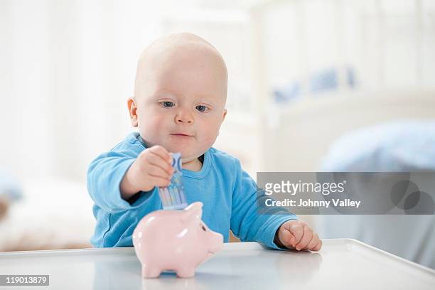 baby boy putting money in piggy bank - save our future babies stock pictures, royalty-free photos & images