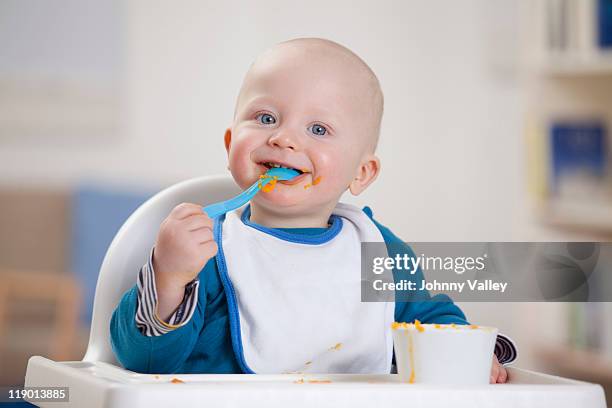 smiling baby boy eating in high chair - spoon stock pictures, royalty-free photos & images