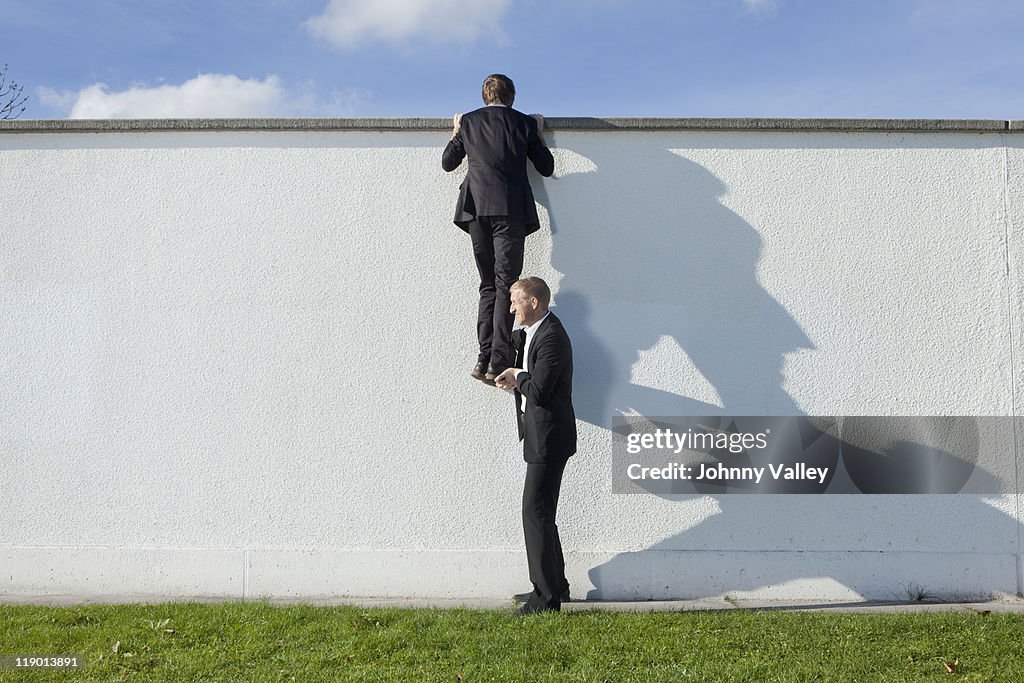 Businessman lifting colleague over wall