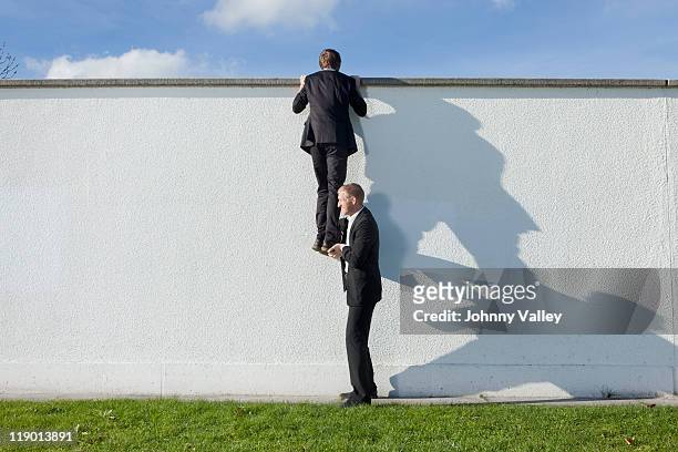 businessman lifting colleague over wall - support stock-fotos und bilder