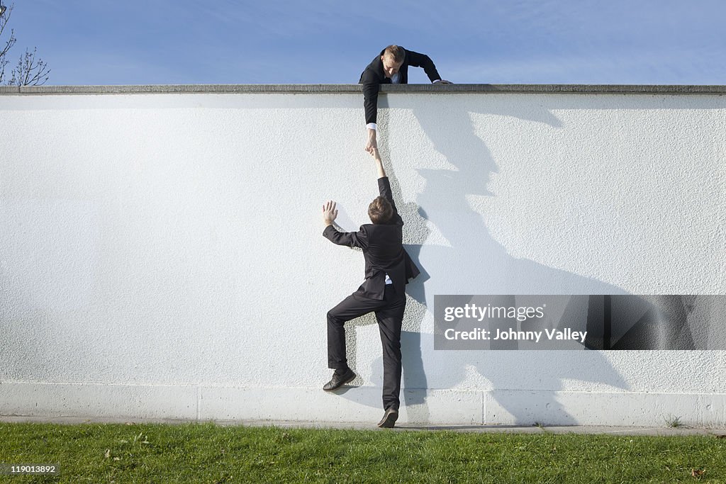 Businessman pulling colleague over wall