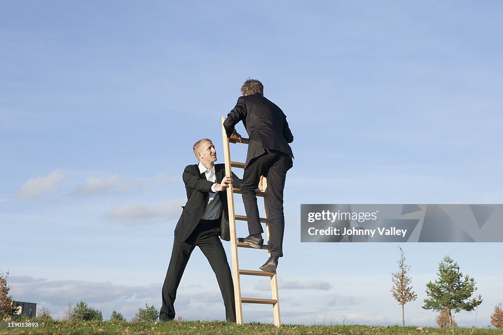 Businessman holding ladder for colleague