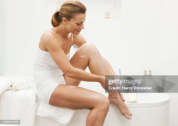 woman moisturizing her legs - beautiful woman bath photos et images de collection