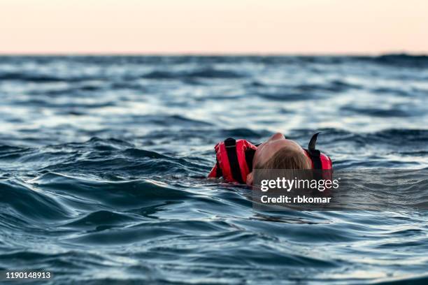 lifeless drowning girl in a life jacket on the high seas at dusk - drowning stock-fotos und bilder